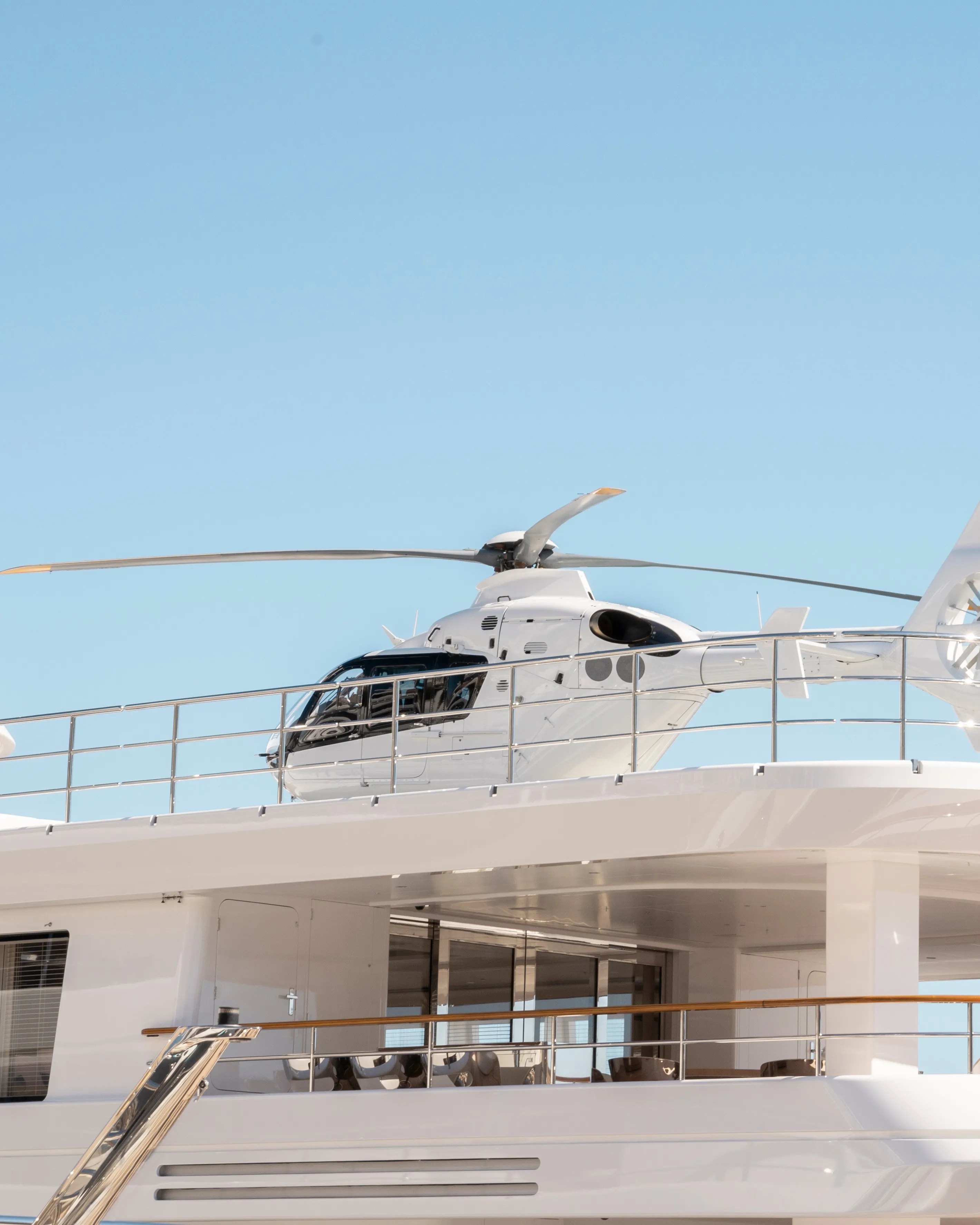 A white helicopter is parked on the upper deck of a motor yacht under a clear blue sky, awaiting the superyacht captain's next command.