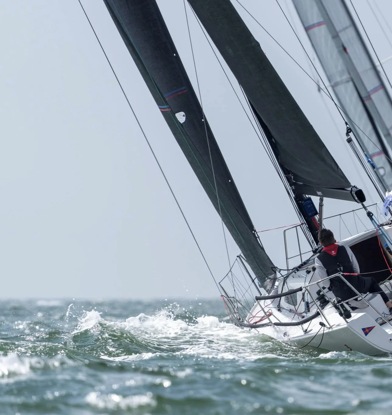 A sailboat with black sails navigates through choppy waters on a clear day during the Round Britain & Ireland Race. Two people are visible managing the boat.