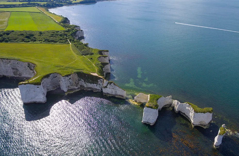 Aerial view of white chalk cliffs and clear blue waters adjacent to green fields along the coastline on a sunny day, a scene that would captivate any superyacht captain.