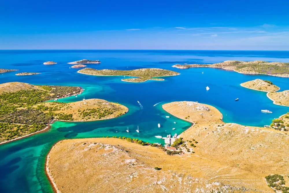 Aerial view of a coastal archipelago, showcasing top sailing destinations with scattered islands, turquoise waters, and boats gliding under a clear blue sky.